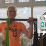 Vrouw kijkt lachend over een pull up bar. Ze staat overduidelijk in een elastiek