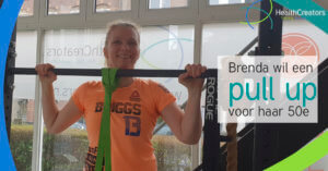Vrouw kijkt lachend over een pull up bar. Ze staat overduidelijk in een elastiek